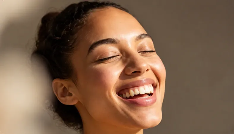 Mujer riendo con los ojos cerrados bajo luz cálida